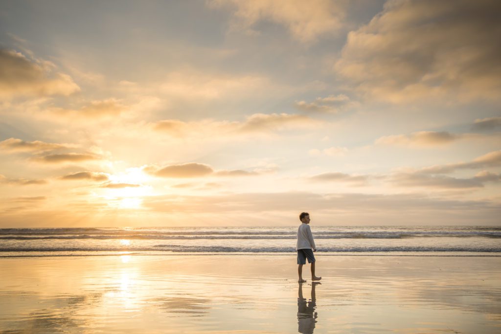 A boy walking on the beach at sunset
