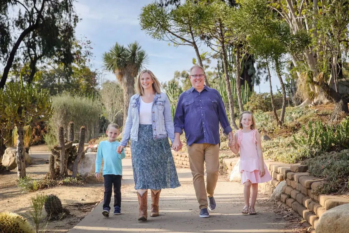Couple walking hand in hand with their two kids poses for a photo on an outdoor park