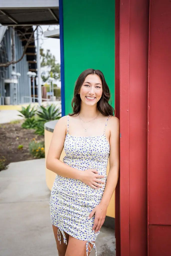 Young woman leaning on a red wall outdoors and wearing a printed short dress