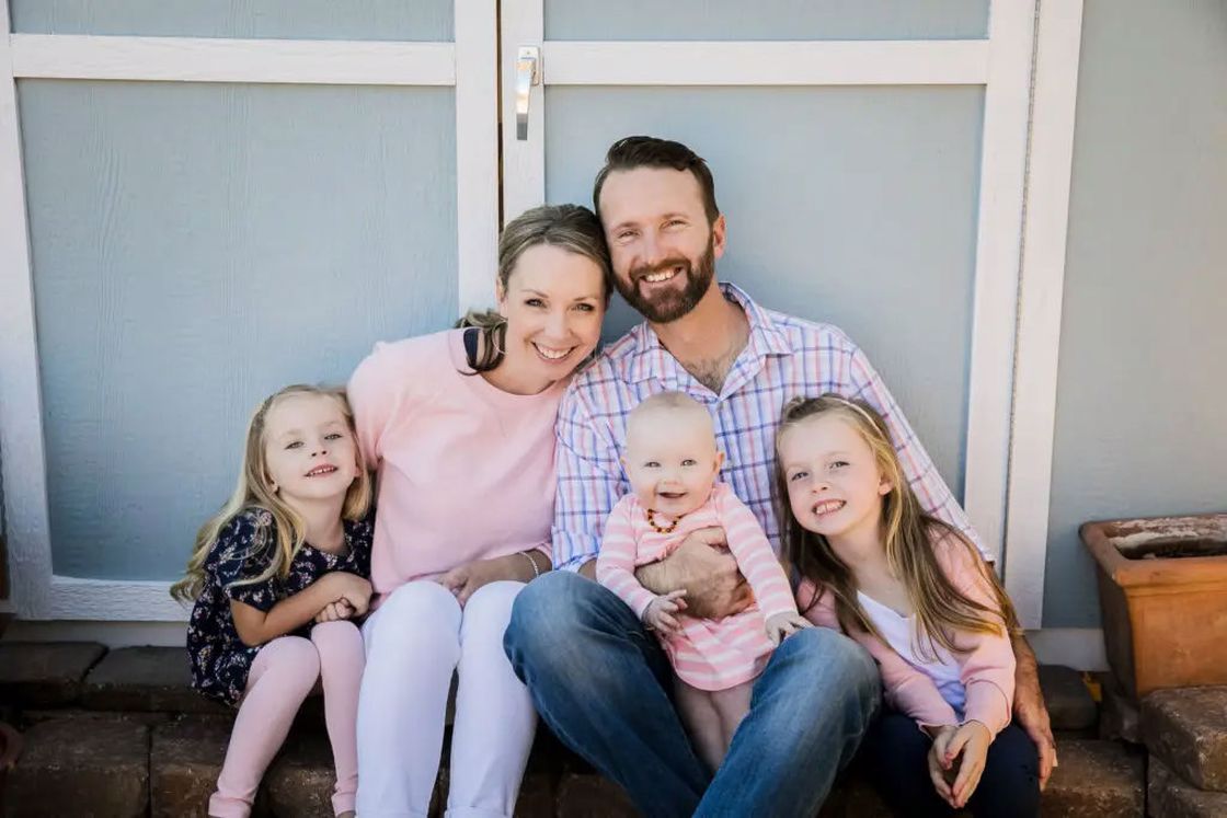 Couple posing with their kids for a family photo while all sitting in front of a blue door