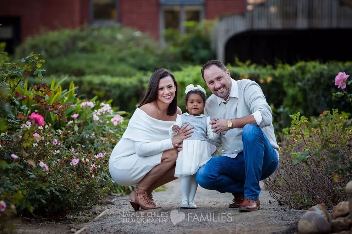 Couple crouching on the paved path while posing with their daughter for a photo