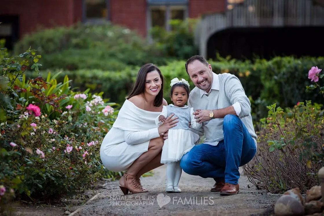 Couple crouching on the paved path while posing with their daughter for a photo