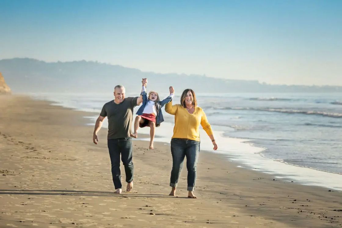 Couple walking on the beach while lifting their little daughter for their photoshoot