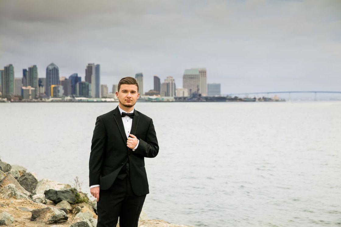 Young man wearing a tuxedo while posing on a beach for his senior photo