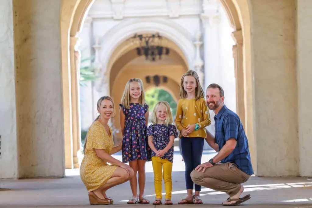 Parents crouching down at the side of their three kids for their family shoot