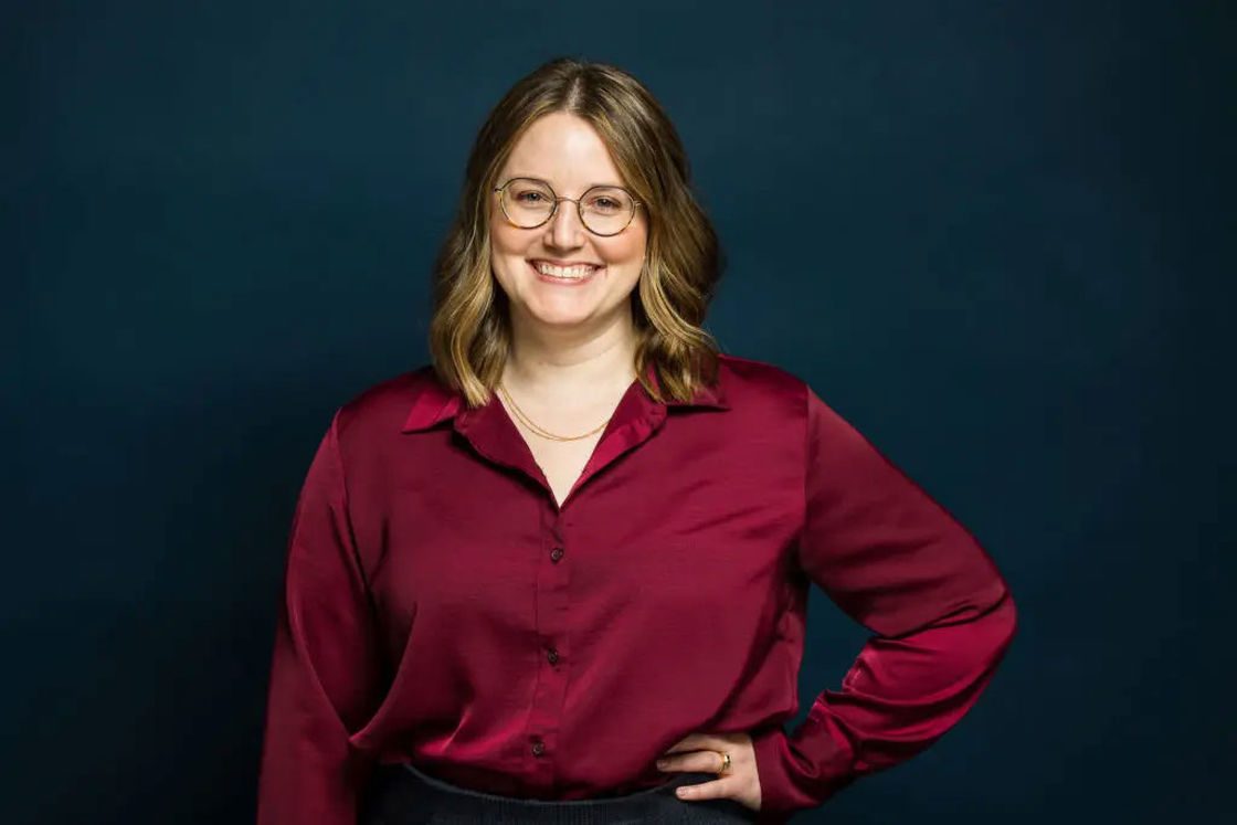 Woman wearing a red silk long-sleeved top as she poses for her headshot with one hand on her hip