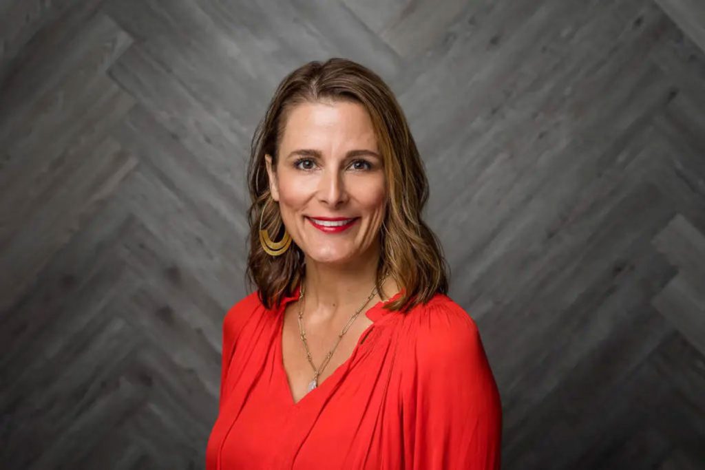 Woman wearing an orange-red top while posing for her headshot