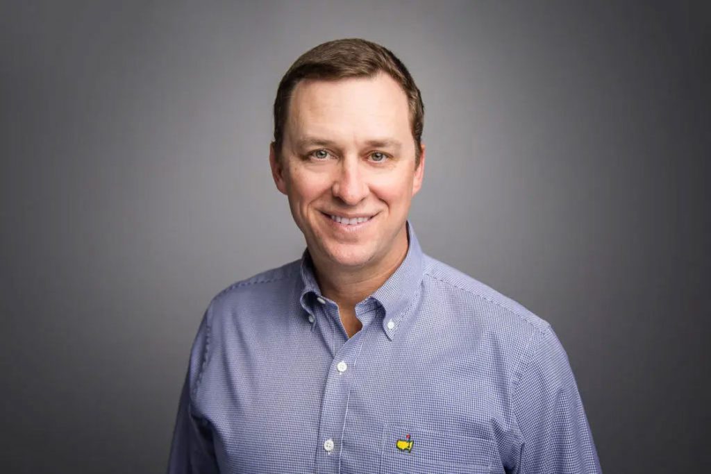 Man wearing a blue long-sleeved dress shirt posing for his headshot with a gray background