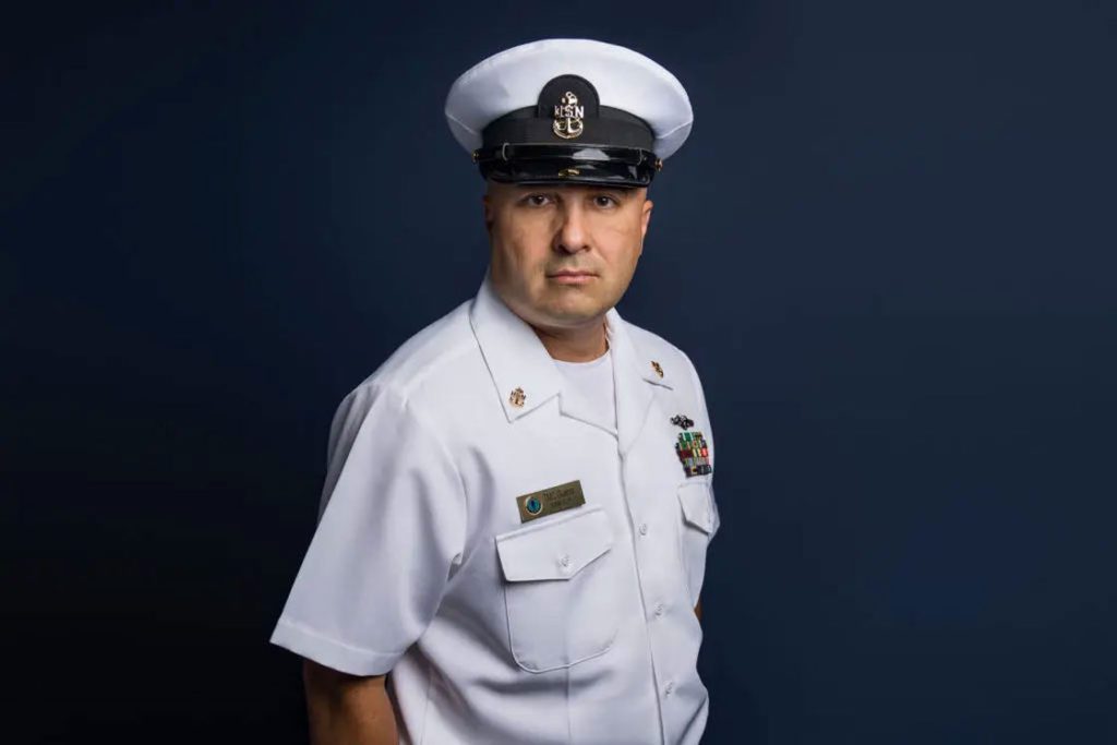 Man wearing his white uniform posing for his headshot with a blue background