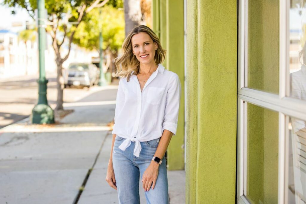 Woman wearing a white buttoned shirt top with blue jeans while posing outside a building for her headshot