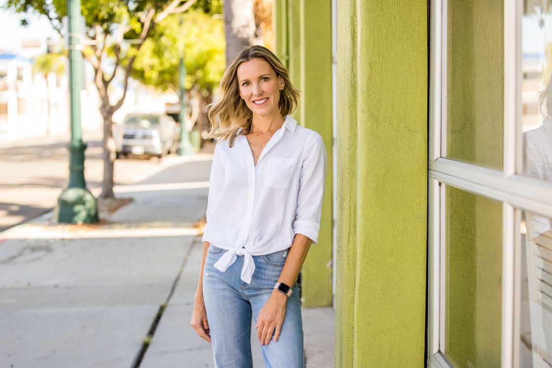 Woman wearing a white buttoned shirt top with blue jeans while posing outside a building for her headshot