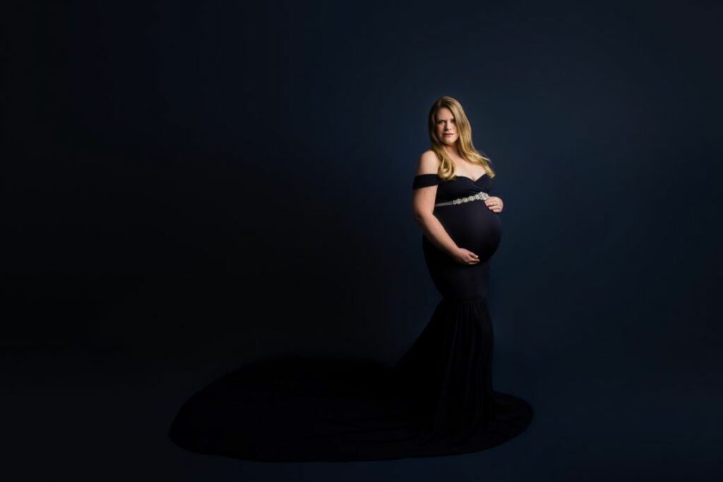 Woman wearing a purple off shoulder dress while clutching her pregnant belly