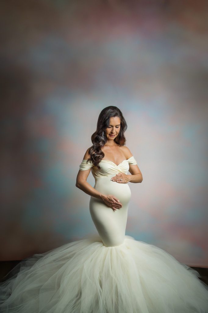 Woman wearing a white long gown while clutching her belly for a maternity shoot