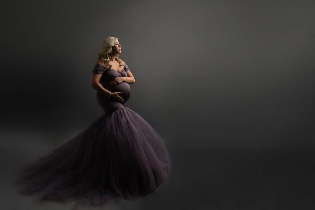 Woman wearing a purple long gown while clutching her belly for a maternity shoot