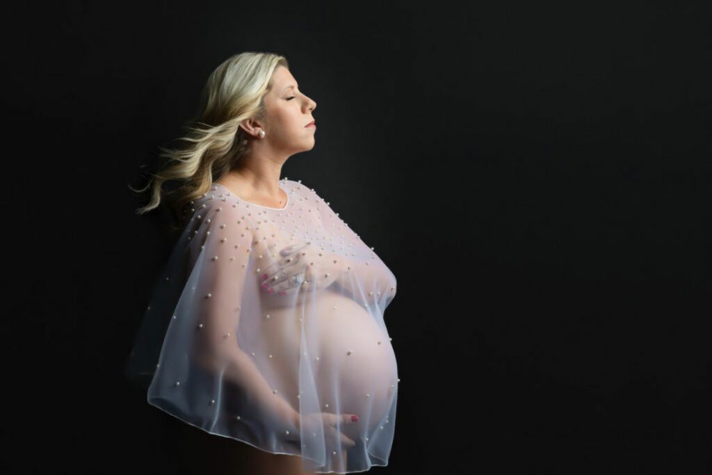 Woman wearing a white see-through top with no undergarments while posing for a maternity shoot