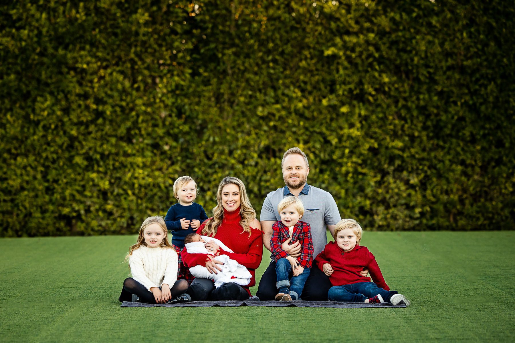 A family sitting on grass with red and blue theme of clothing