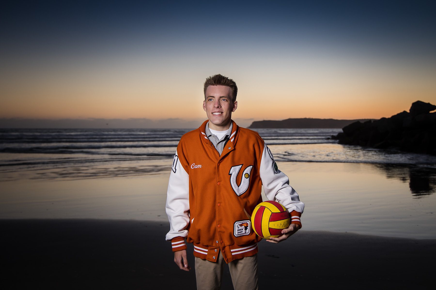A young man in an orange and white jacket holds a volleyball