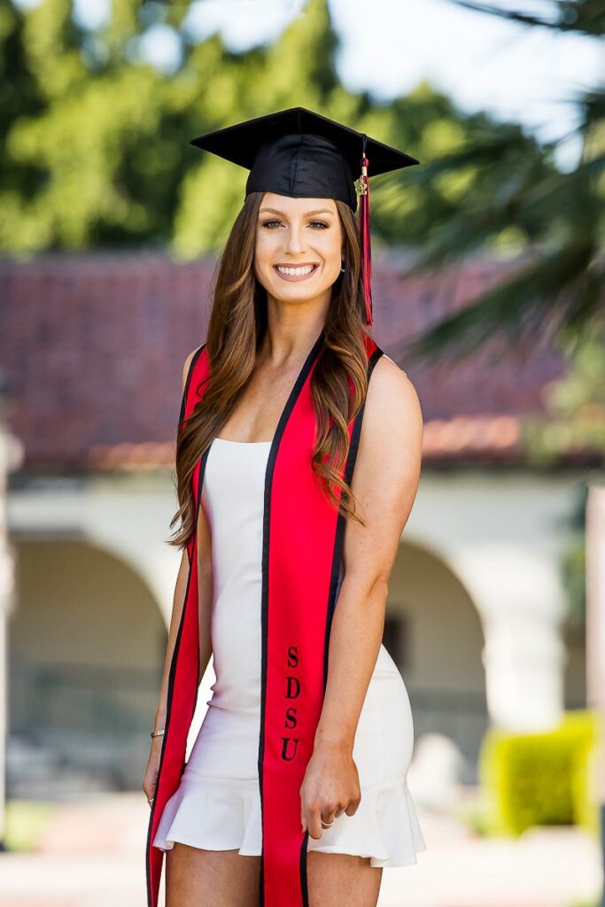 A young woman in a graduation gown and a red and black cap smiles proudly on her graduation day