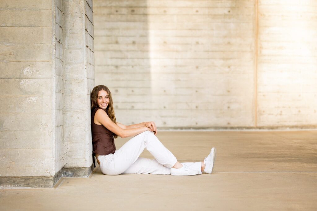 Teen girl sitting on the ground in front of a concrete wall, smiling