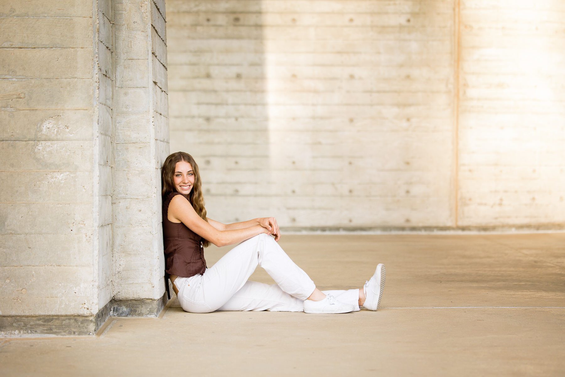 Teen girl sitting on the ground in front of a concrete wall, smiling