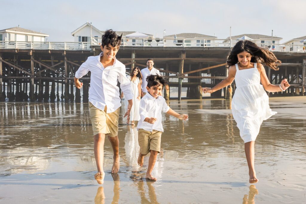 A family of four running along the beach with a pier in the background