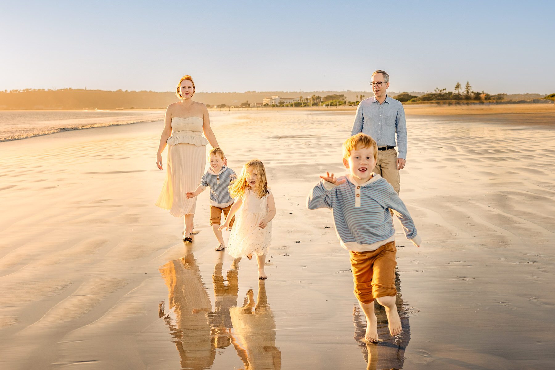 A family of five walking along a sandy beach with the sun setting in the background